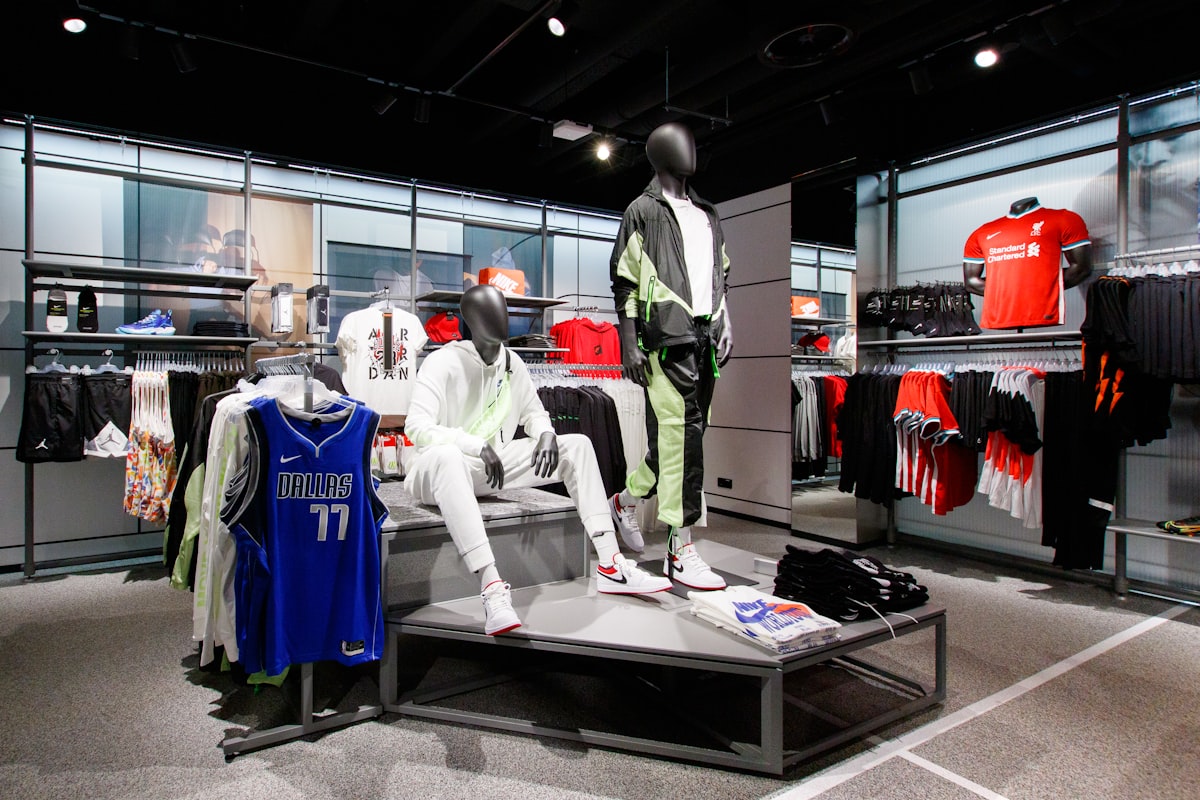 Interior de loja de artigos esportivos com manequins, camisetas e tênis em exposição